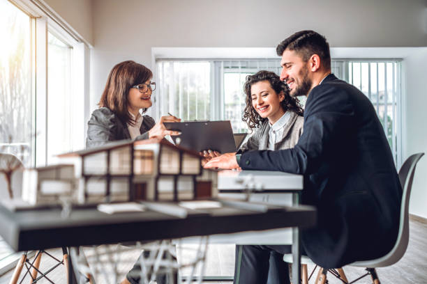 Side view image of young happy family sitting in consulting office, making property purchase. Mature female realtor helping business couple do financial investment. Installment payment, mortgage, loan for estate concept